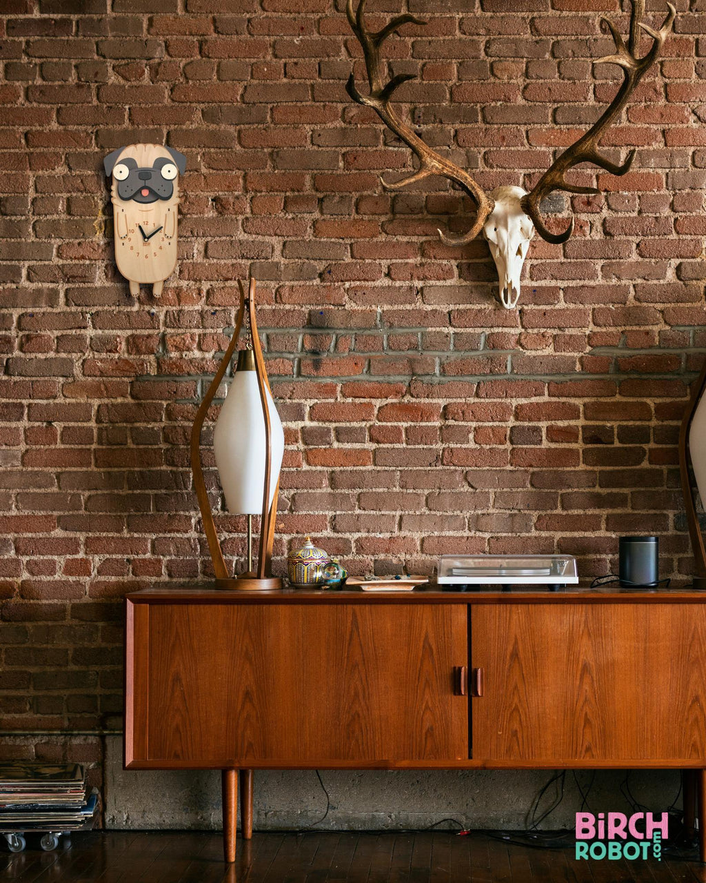 Handcrafted dog wall clock on exposed brick bedroom wall with modern decor and antler mount.